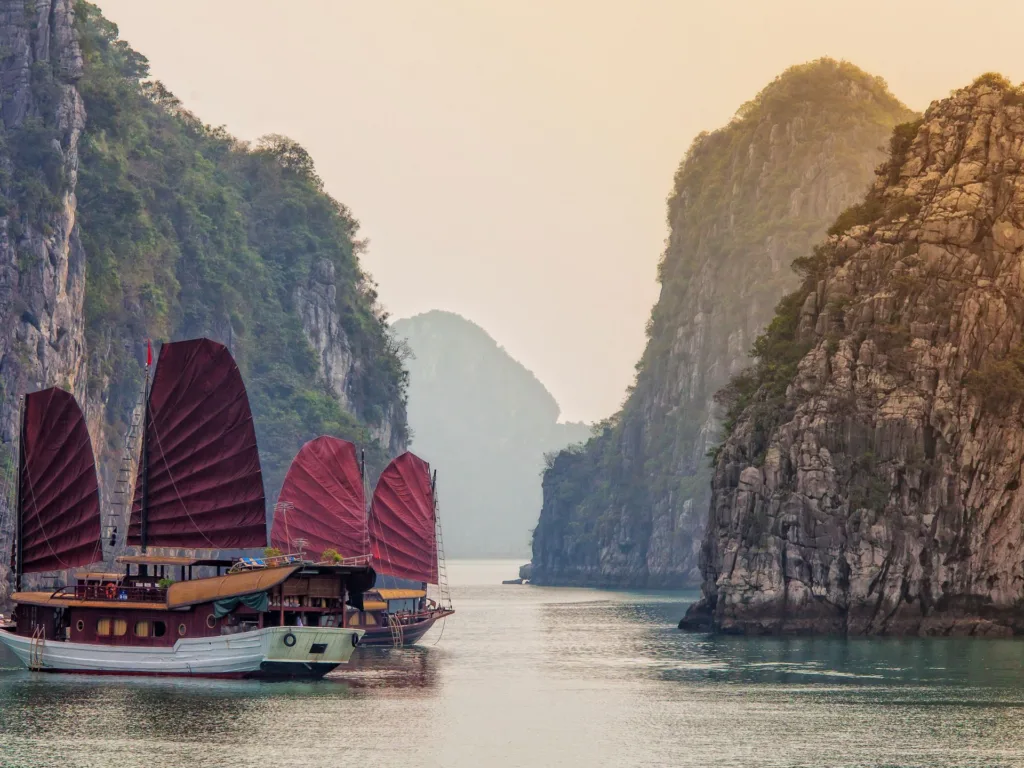 A landscape view of the karst peaks in Ha Long Bay, Vietnam with traditional junk ships in the water.